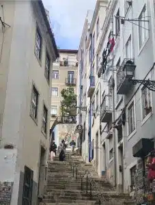 Rua íngreme em Mouraria, Lisboa, com escadas, roupa estendida no estendal, lojas e pessoas a passear pelo bairro.