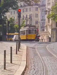 O tradicional elétrico amarelo de Lisboa aproxima-se, percorrendo os trilhos curvos no centro histórico da cidade.