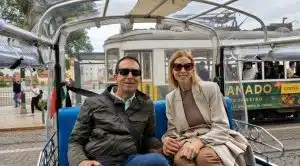 Couple enjoying a private tuk tuk tour in Lisbon with a traditional yellow tram in the background.